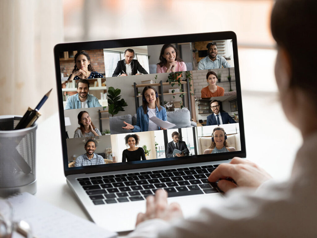 Someone sitting at a laptop computer and participating in a virtual office meeting.