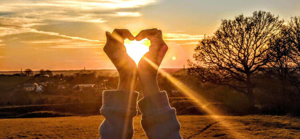 sun shining through cupped hands in the shape of a heart