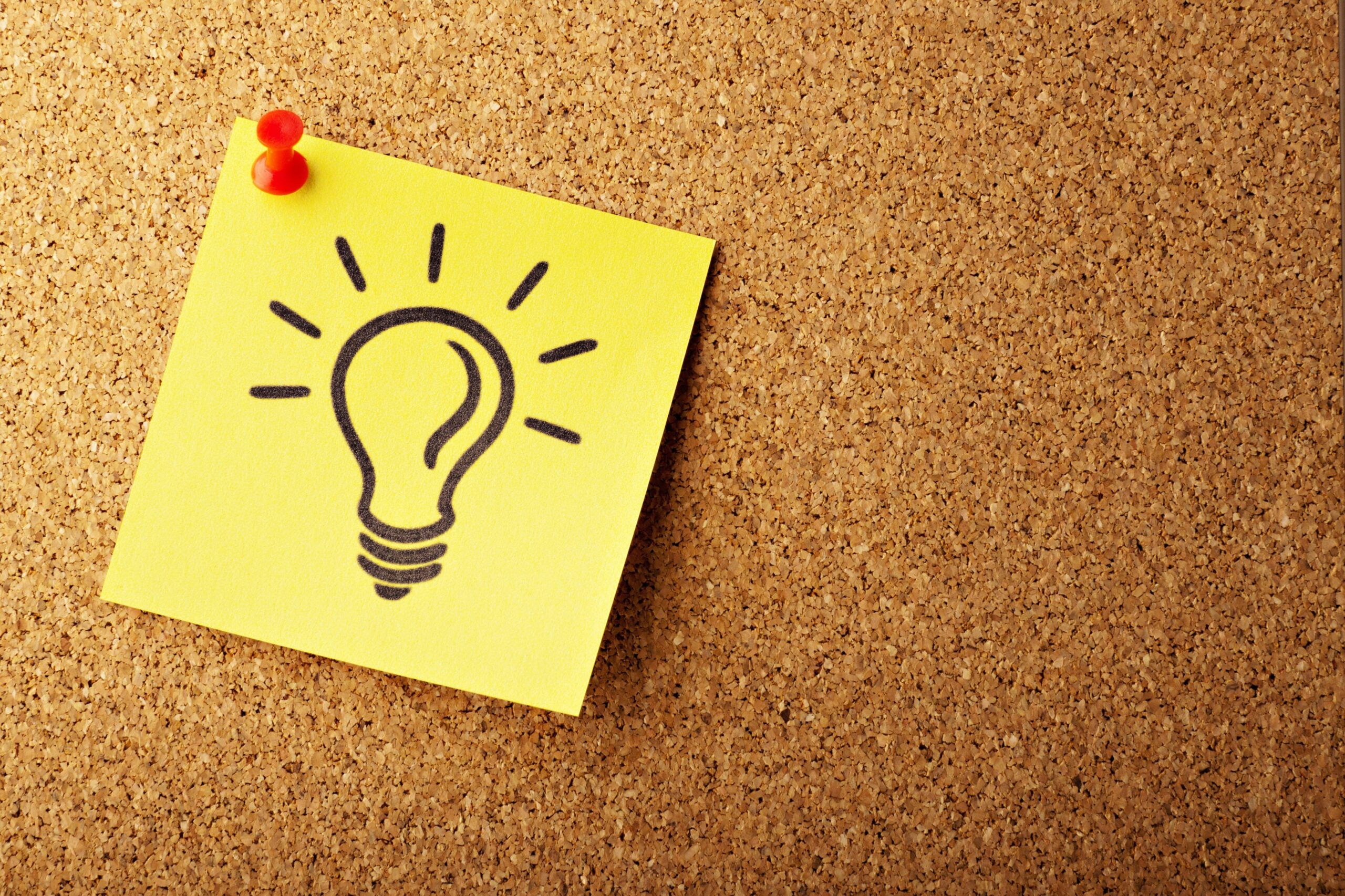 Yellow sticky note with an illustration of a light bulb pinned to a cork board.