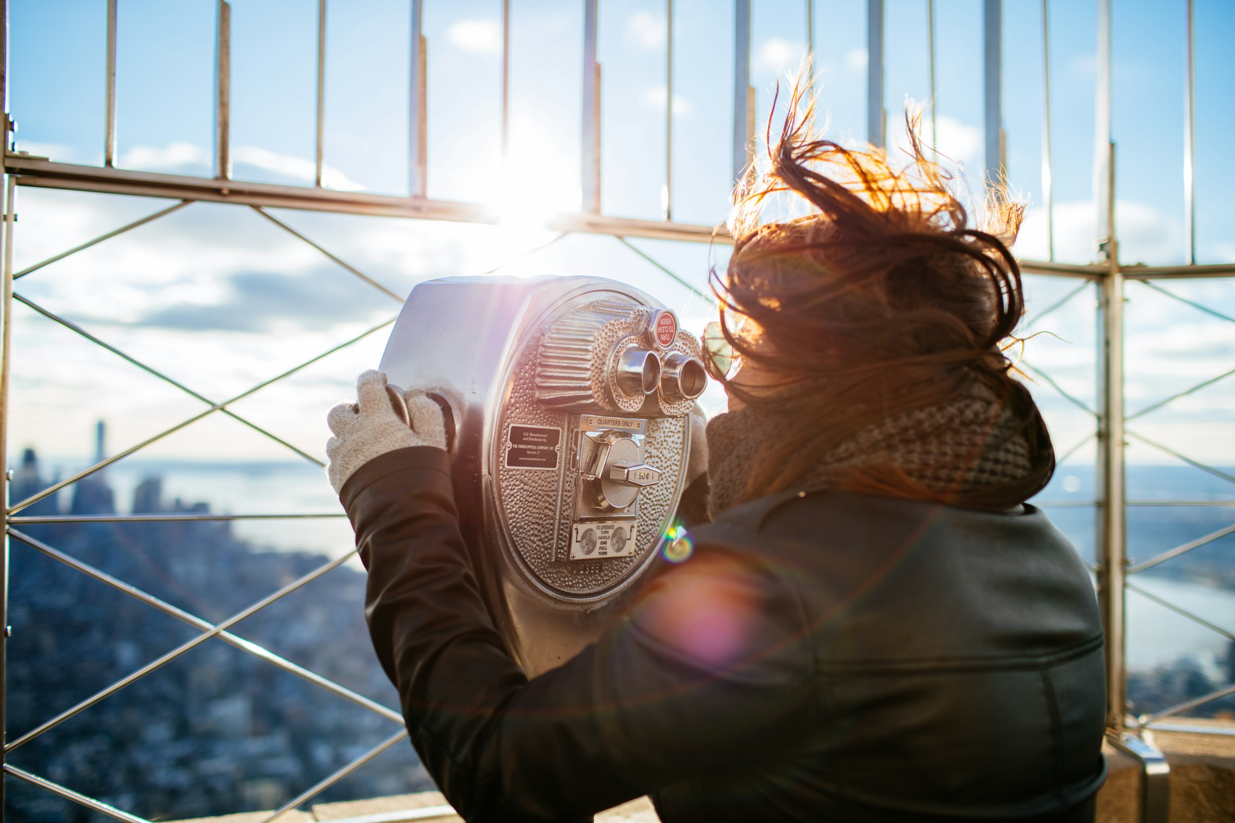 A woman looking through a telescope on the Empire State building on a windy day.