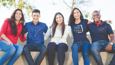 Group of young people sitting on a wall laughing.