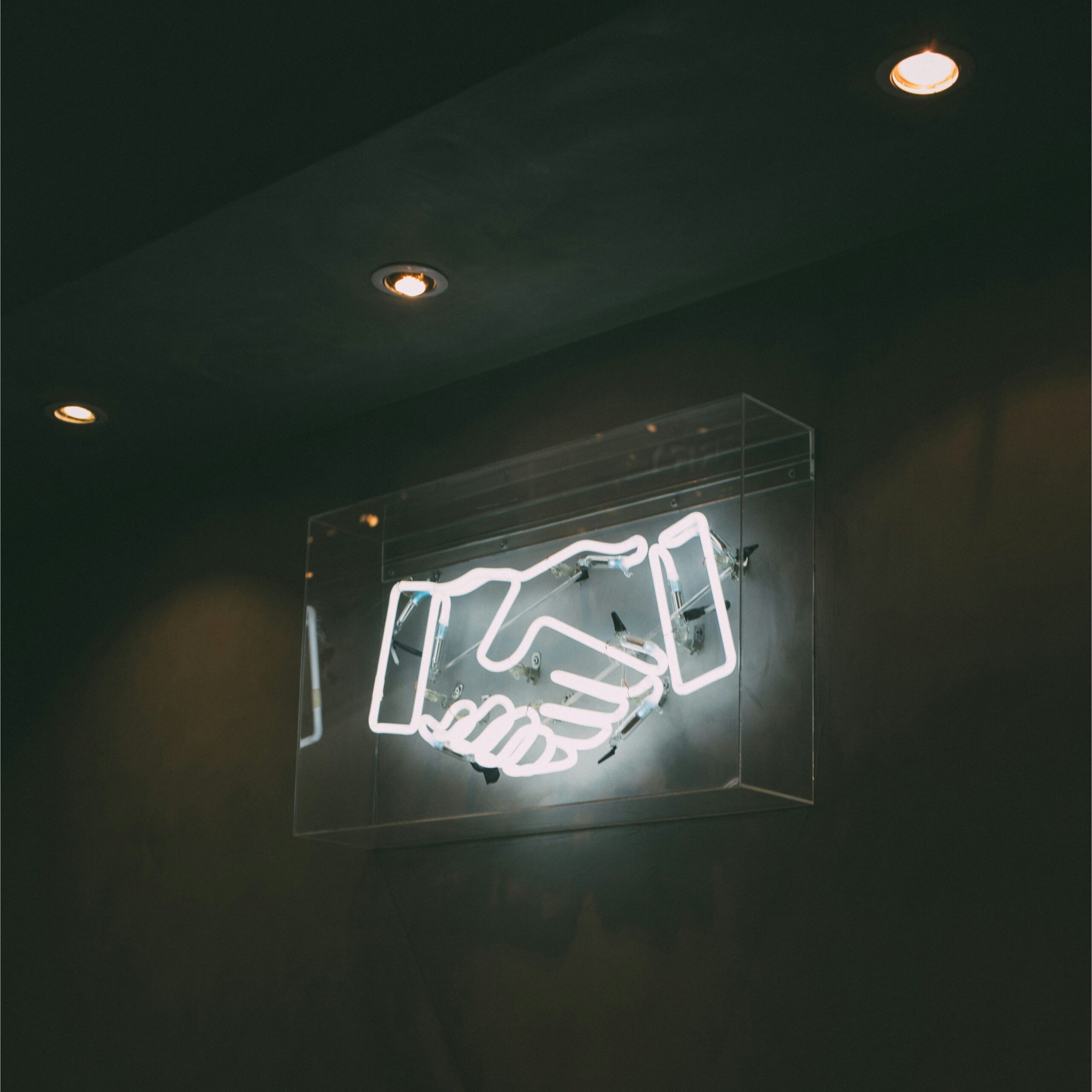 White neon sign of shaking hands on a dark colored wall.