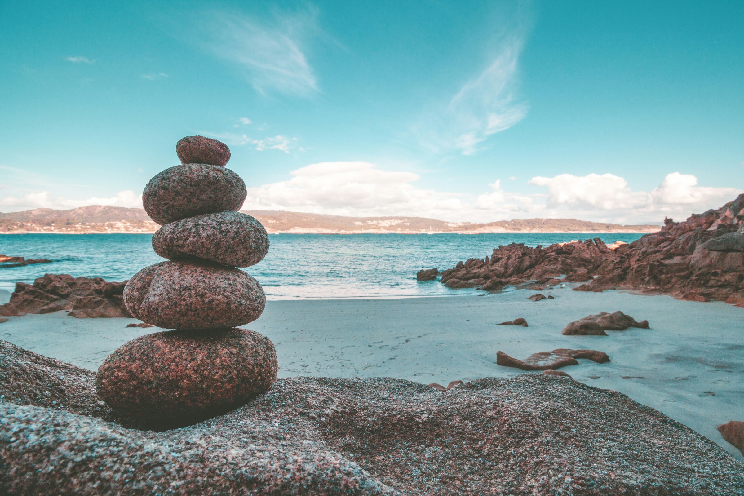 A cairn of five small granite rocks on granite boulder on a lake shore.