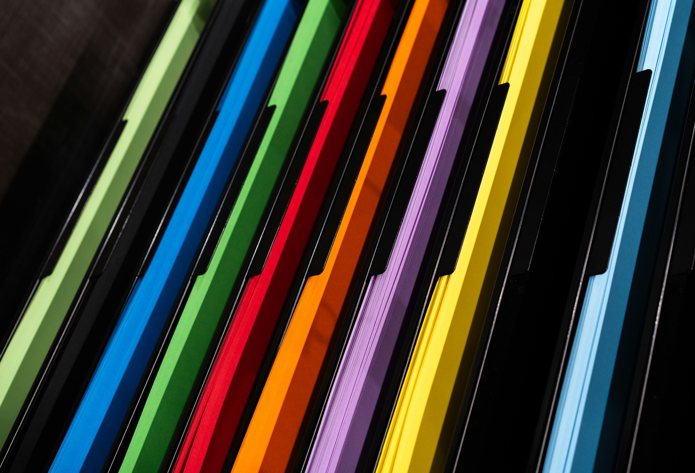 9 brightly colored letter sized binders standing upright with their edges facing the camera.