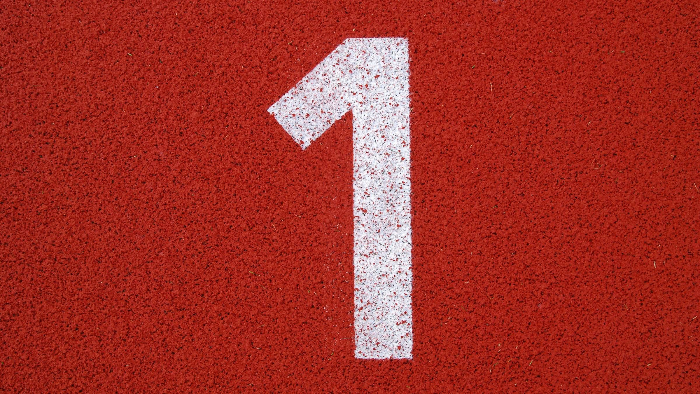 Close up of a number 1 in white paint on a red running track.