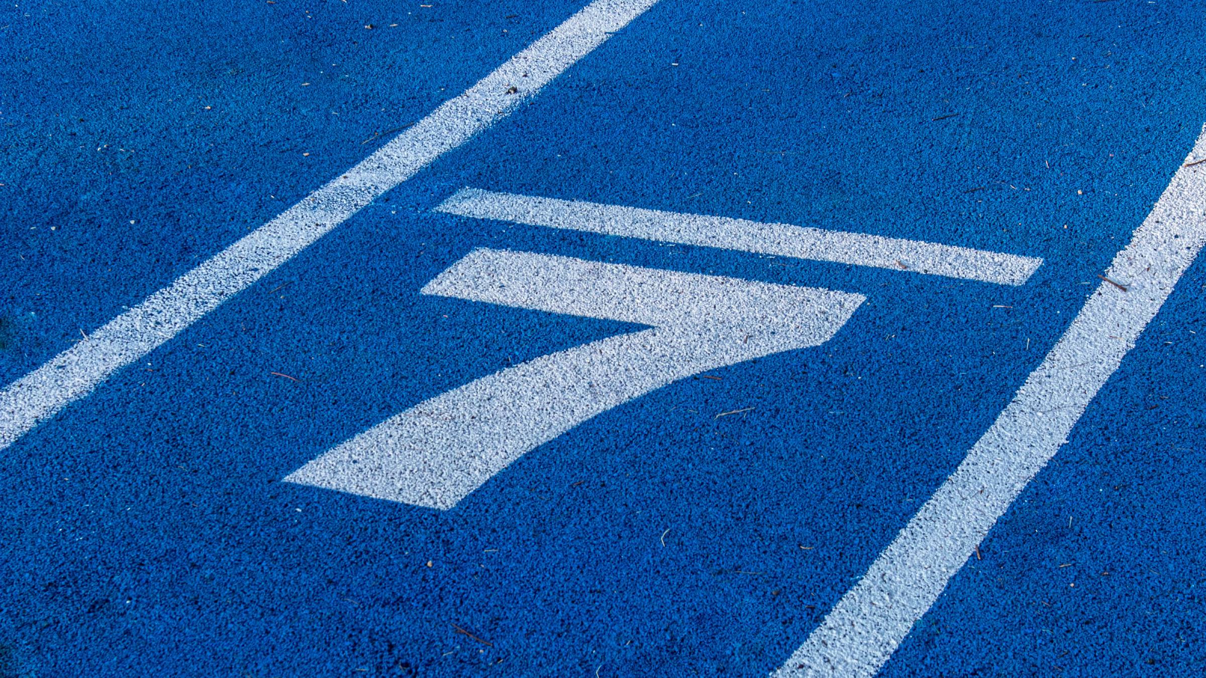 Close up of a number 7 in white paint on a blue running track.
