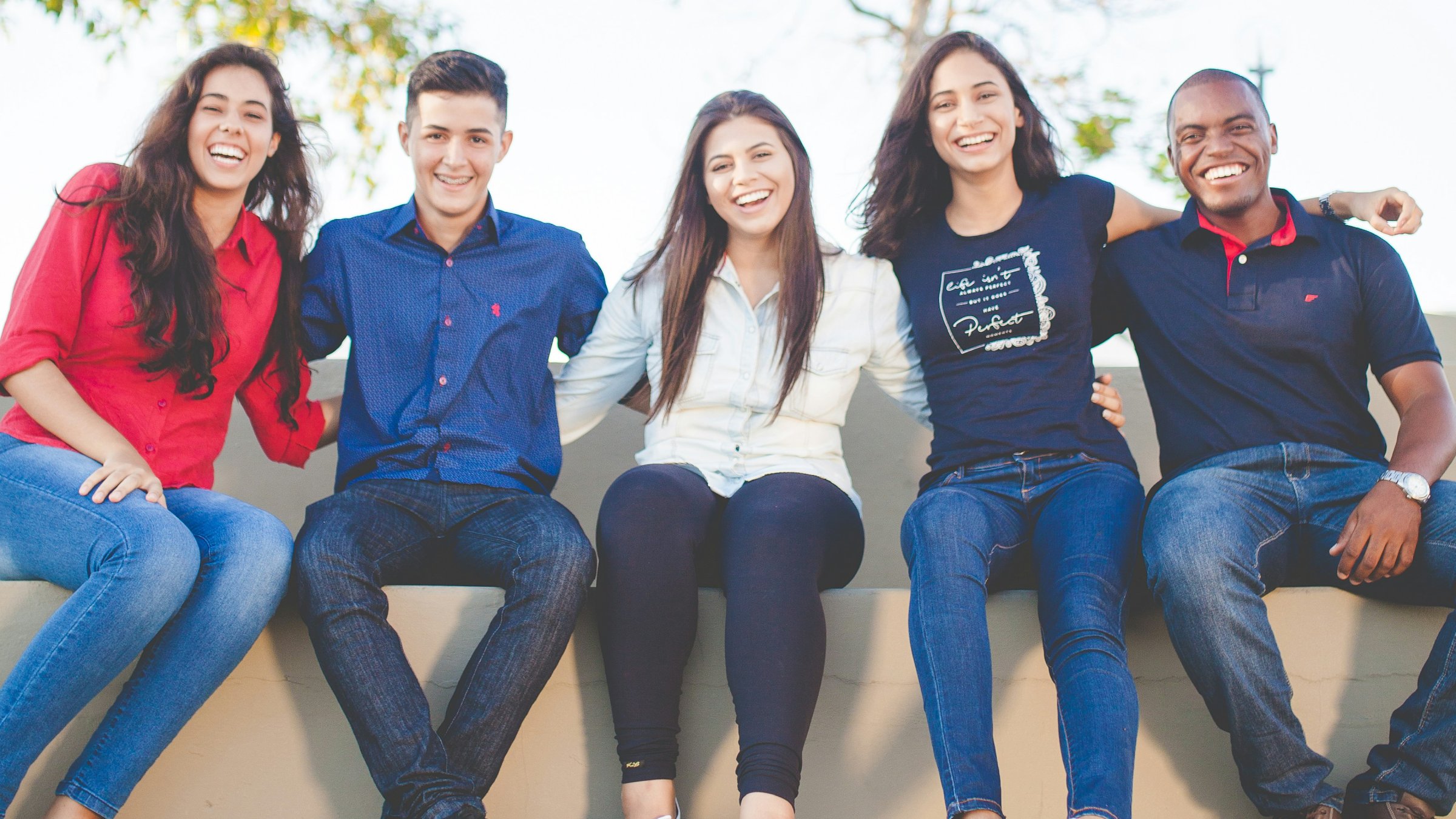 Group of young people sitting on a wall laughing.