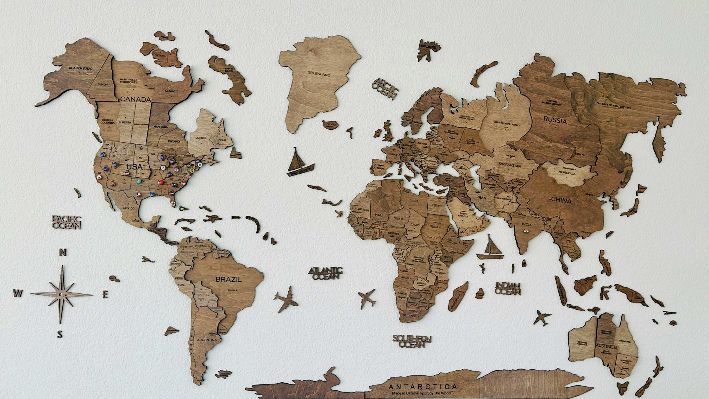 Wooden jigsaw map of the world with continents, ocean names, planes, and boats.