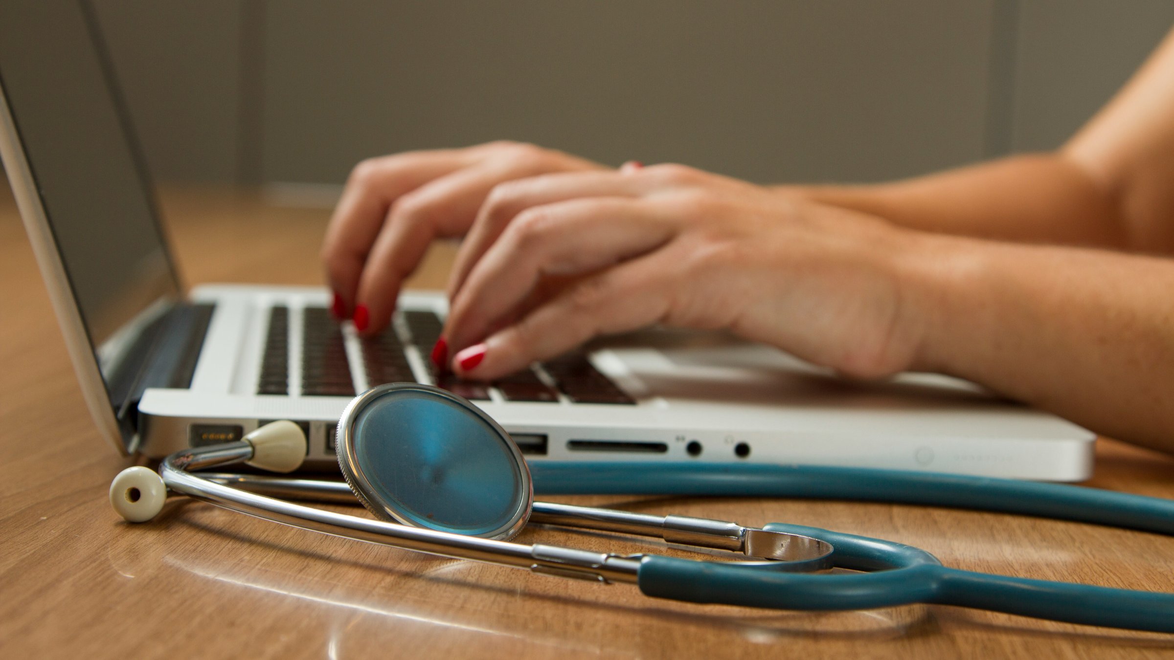 Close up of a stethoscope sitting on a desk with a laptop in the background.