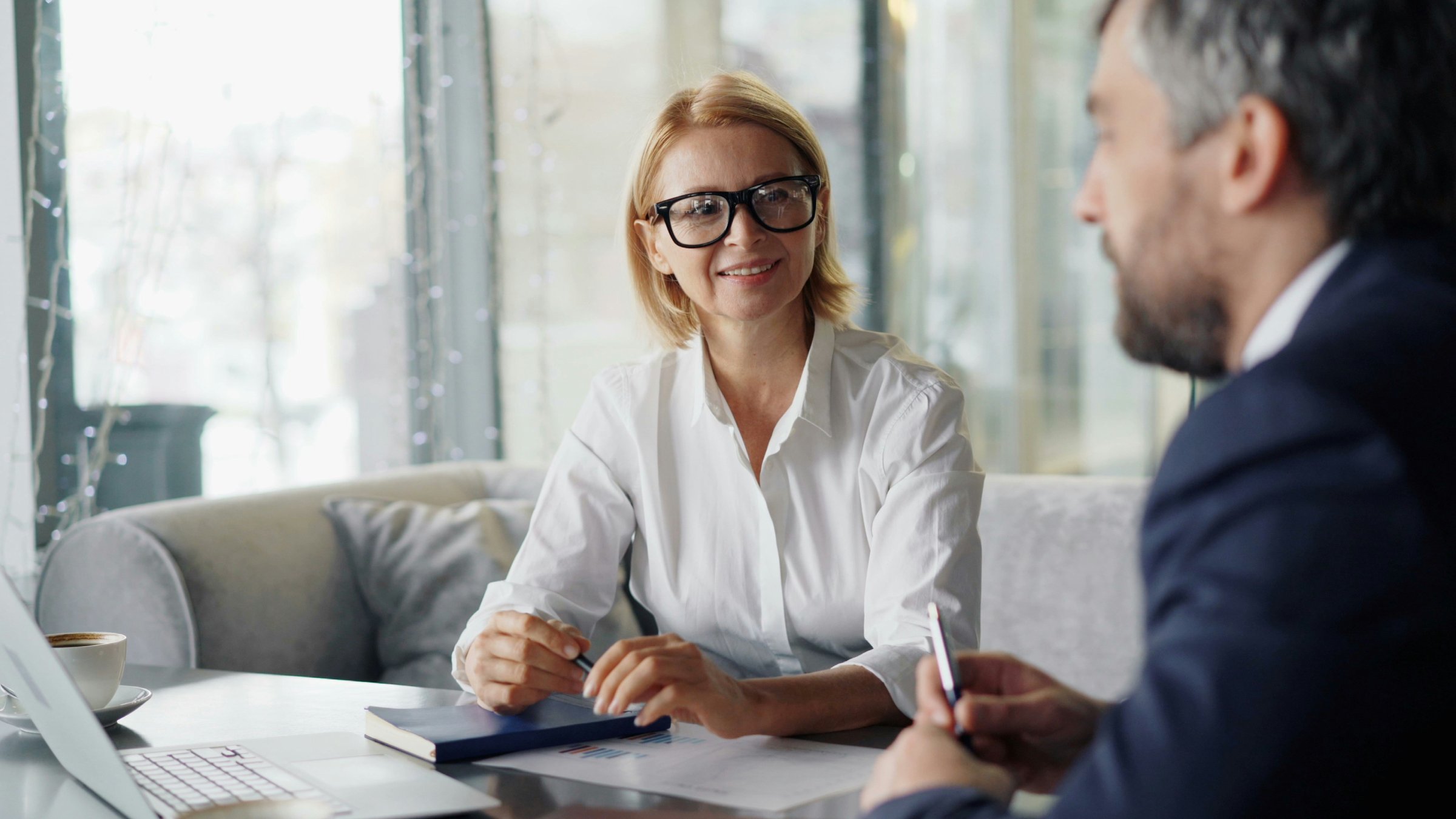 A man and a woman sitting at a coffee table talking and smiling.