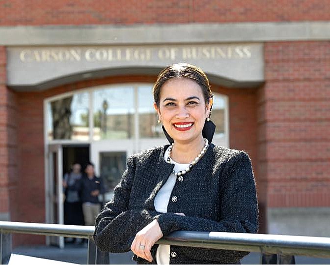 A photo of a woman smiling in front of a university building.