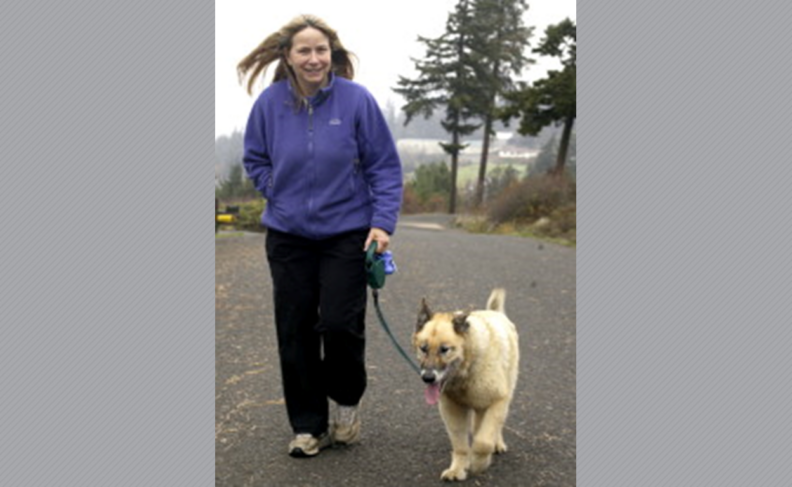 Cindy Anderson in a purple fleece, walking a dog outside.