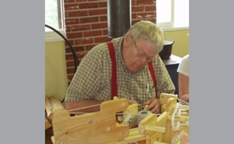 William Burris in red suspenders and a plaid shirt sitting at a table.