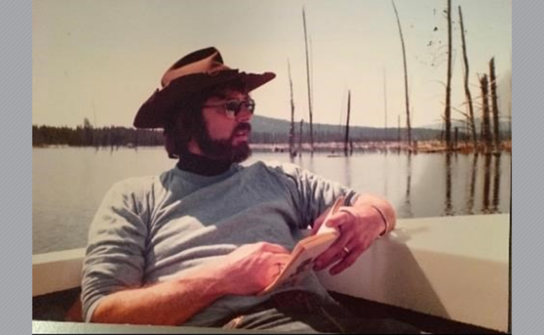 Photo of Peter Davis reading a book on a lake.