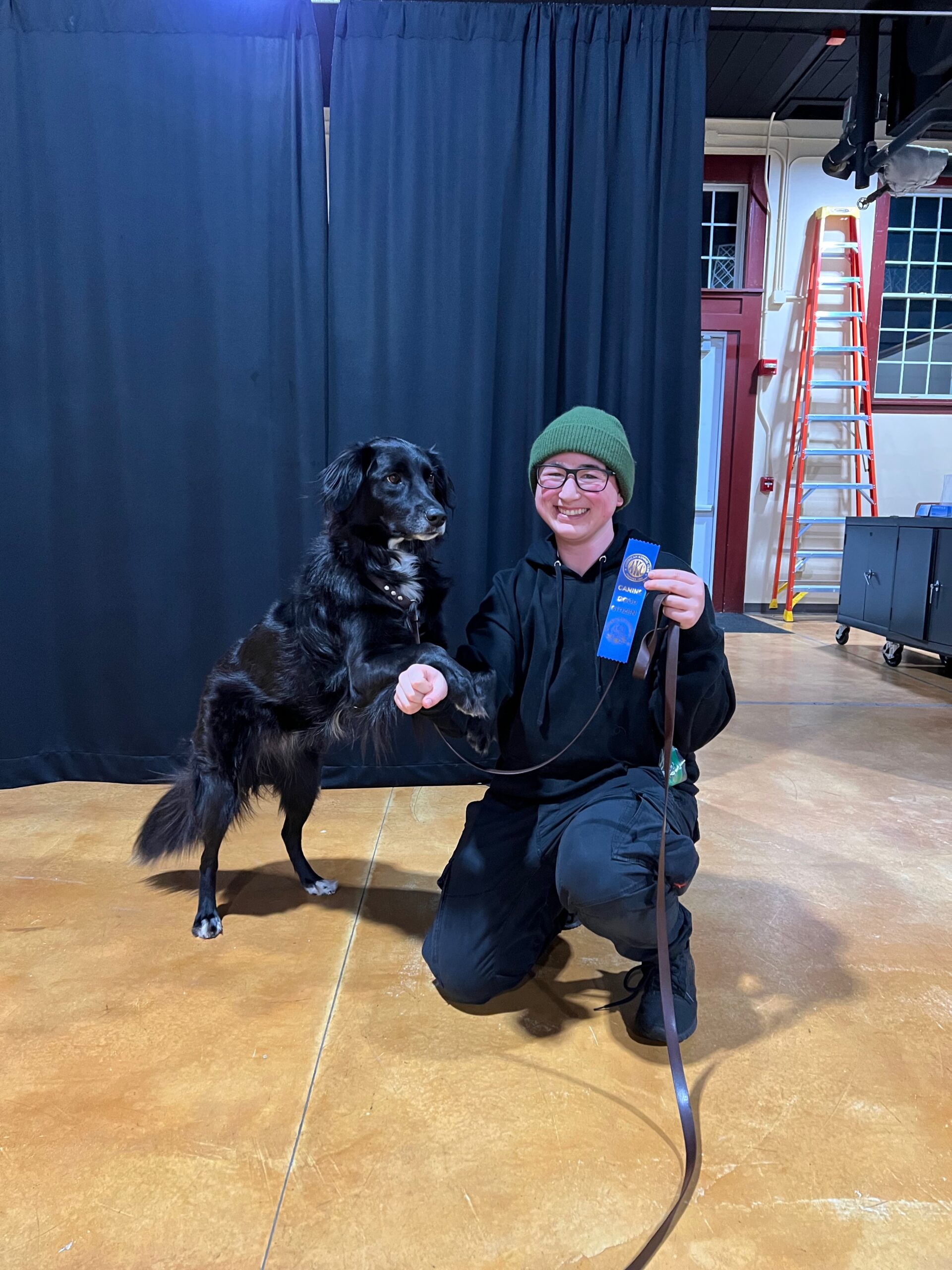 A dog owner holds their dog displaying their blue ribbon after completing the canine good citizen test.