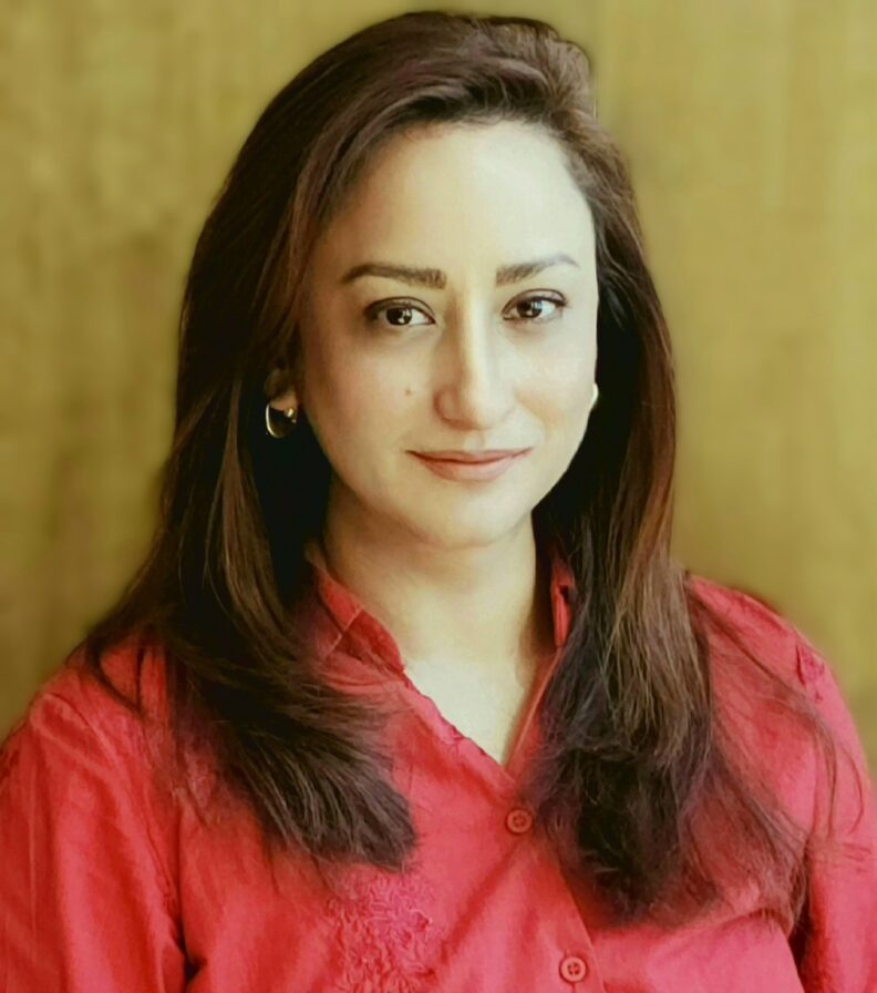 A close-up portrait of a person wearing a red blouse, facing the camera, with long dark hair and a neutral-toned background.