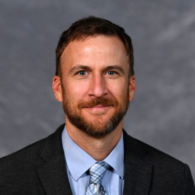 Close-up portrait of Edward R. Murrow College of Communication Professor Benjamin Shors in a black suit with a gray background