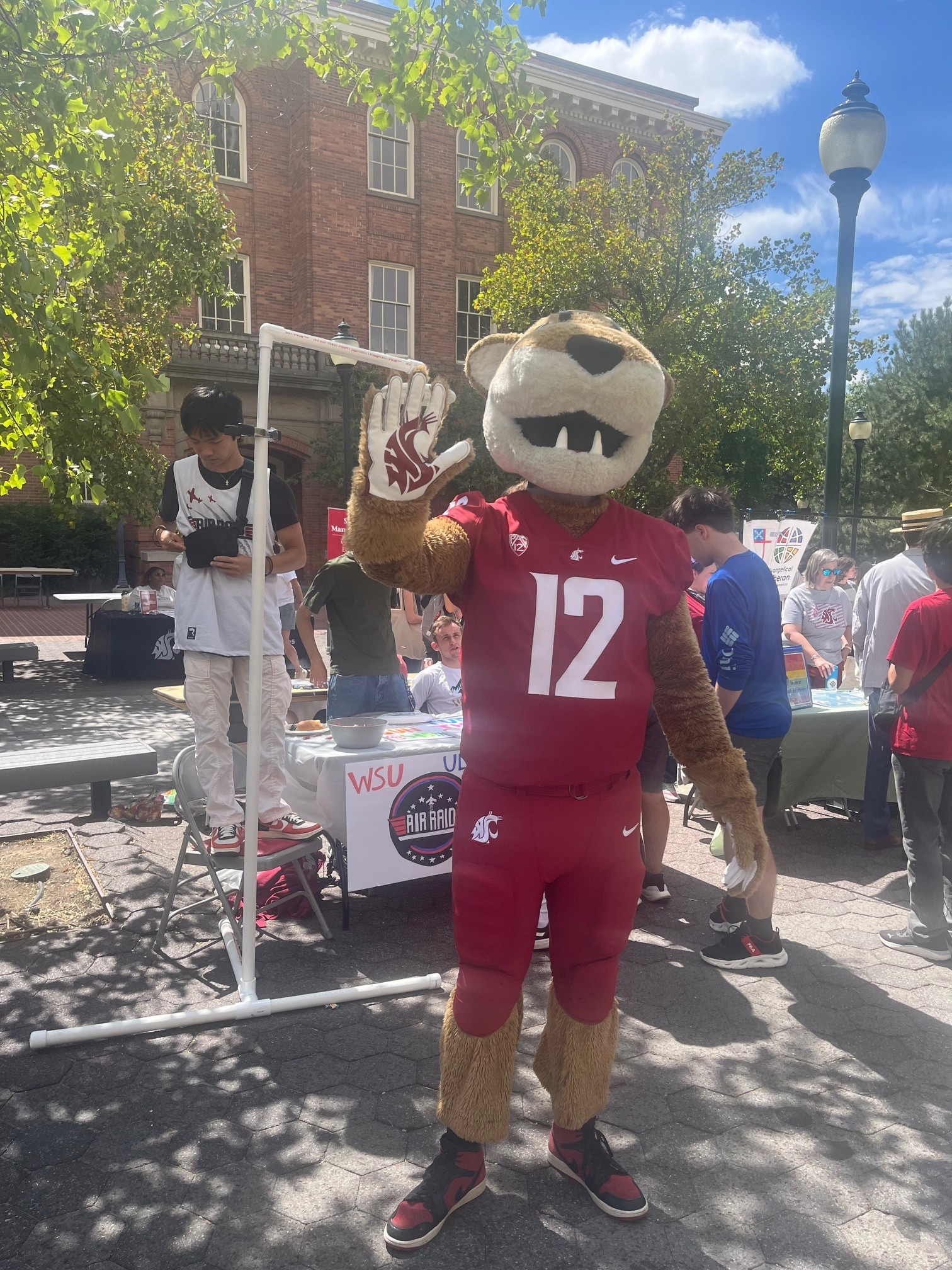 WSU mascot Butch T. Cougar in a #12 jersey waves at the camera during a campus event.