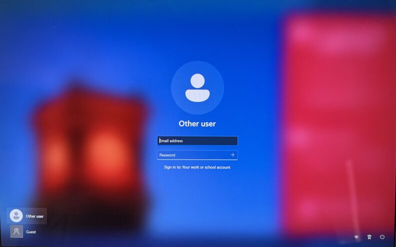 Windows sign‑in screen labeled ‘Other user’ with fields for ‘Email address’ and ‘Password’ to sign in to a work or school account. Options for ‘Other user’ and ‘Guest’ are shown.