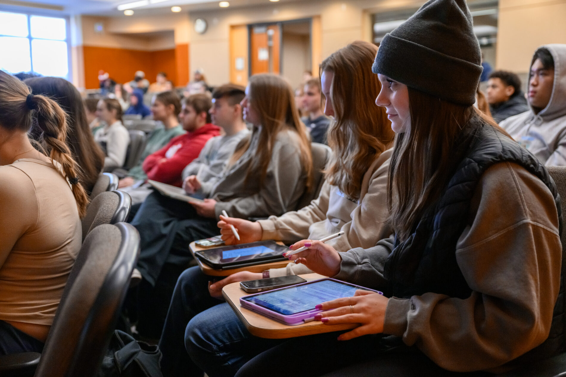 Students seated in a lecture hall, attentively listening and taking notes on tablets with styluses during a class session.