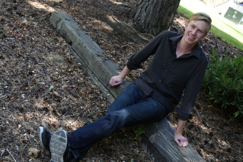 Dustin Van Orman sitting on the ground while smiling upward at the camera.