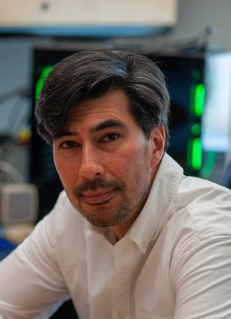 Dr. Driskell leaning on a desk. He's seated and wearing a white button up shirt.