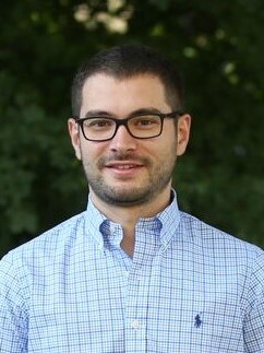 A portrait of Cihan Demir against a leafy backdrop.
