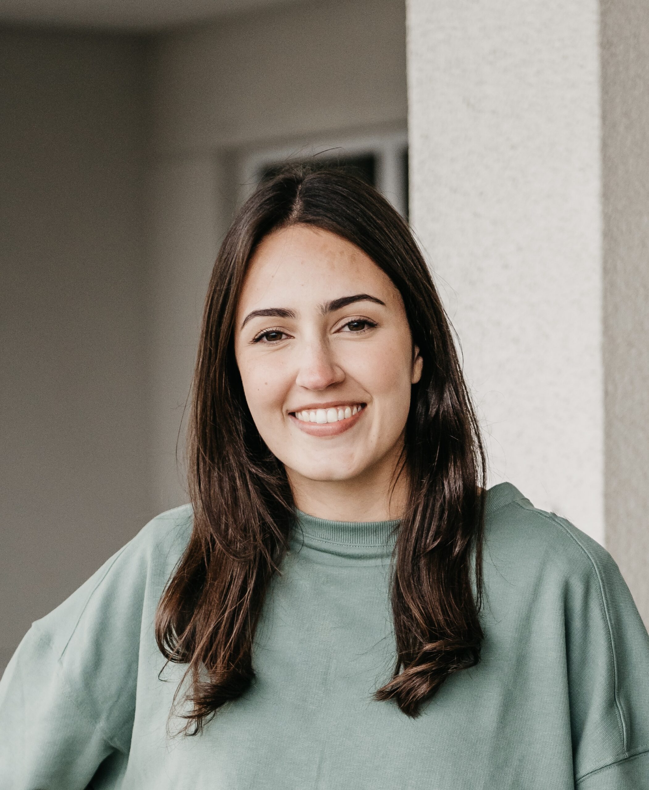 A portrait of Laura Pires Gifford standing against a white wall.