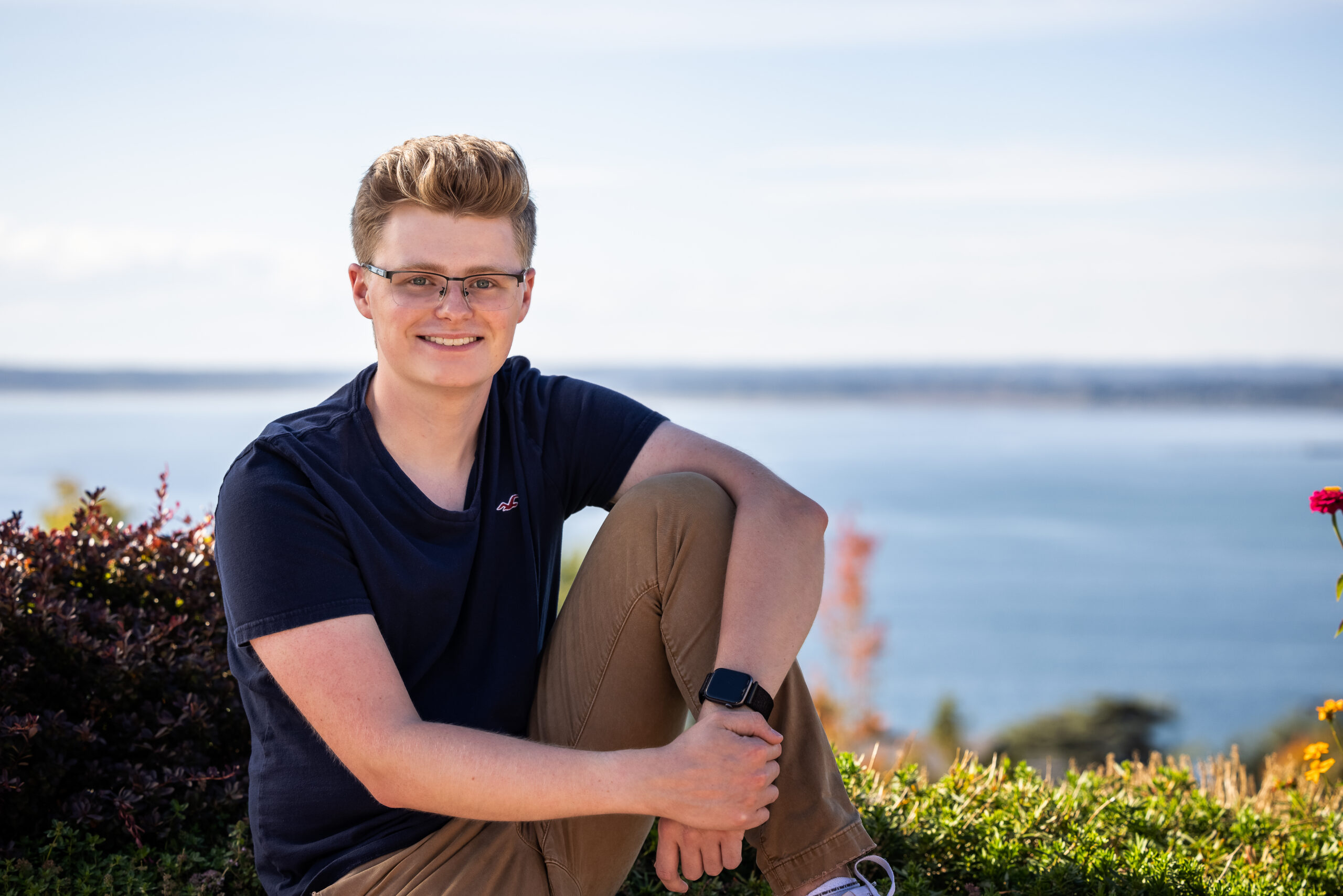 A portrait of Jackson Graddon sitting on a ledge against an ocean backdrop.