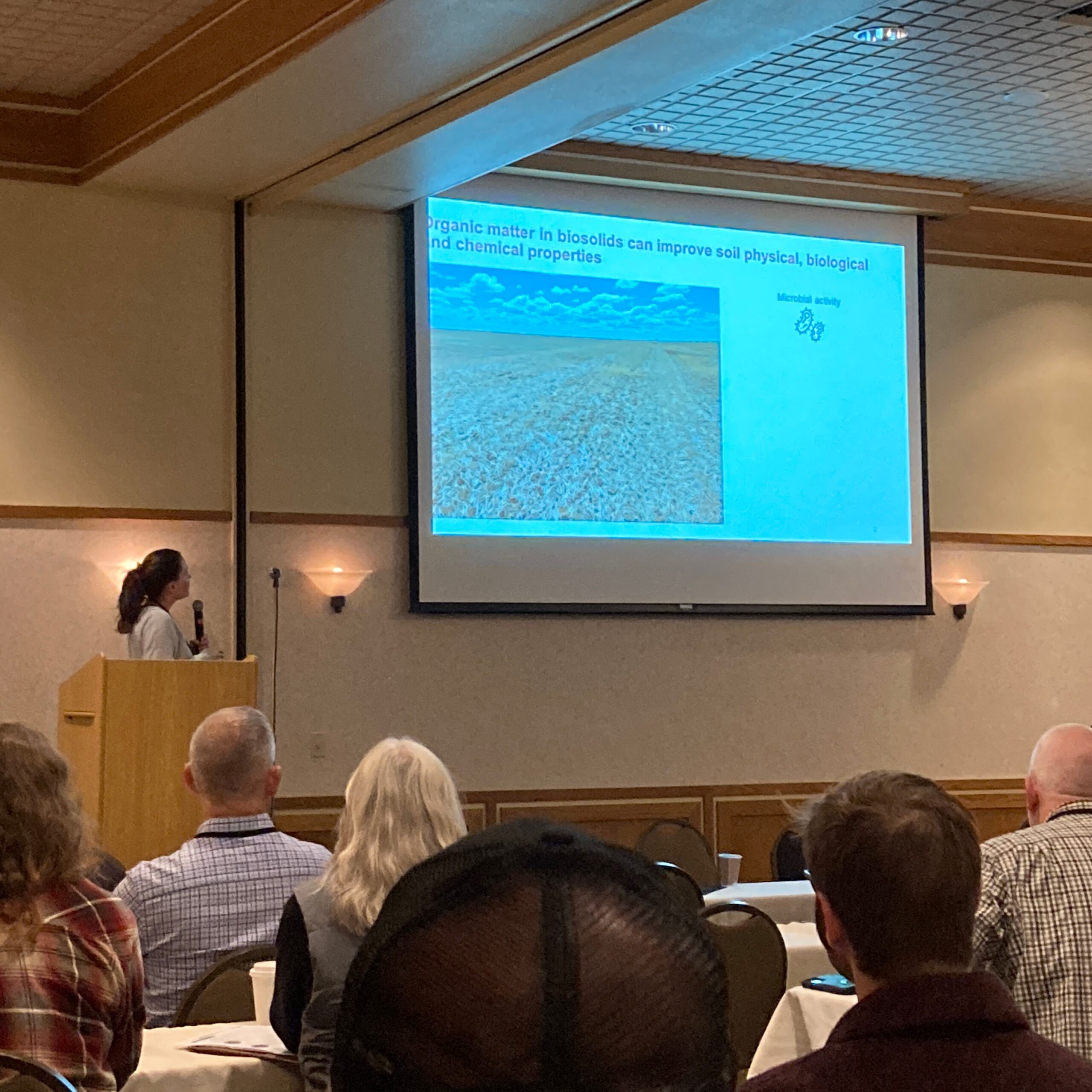 Deirdre presents to an audience, with slides projected behind her.