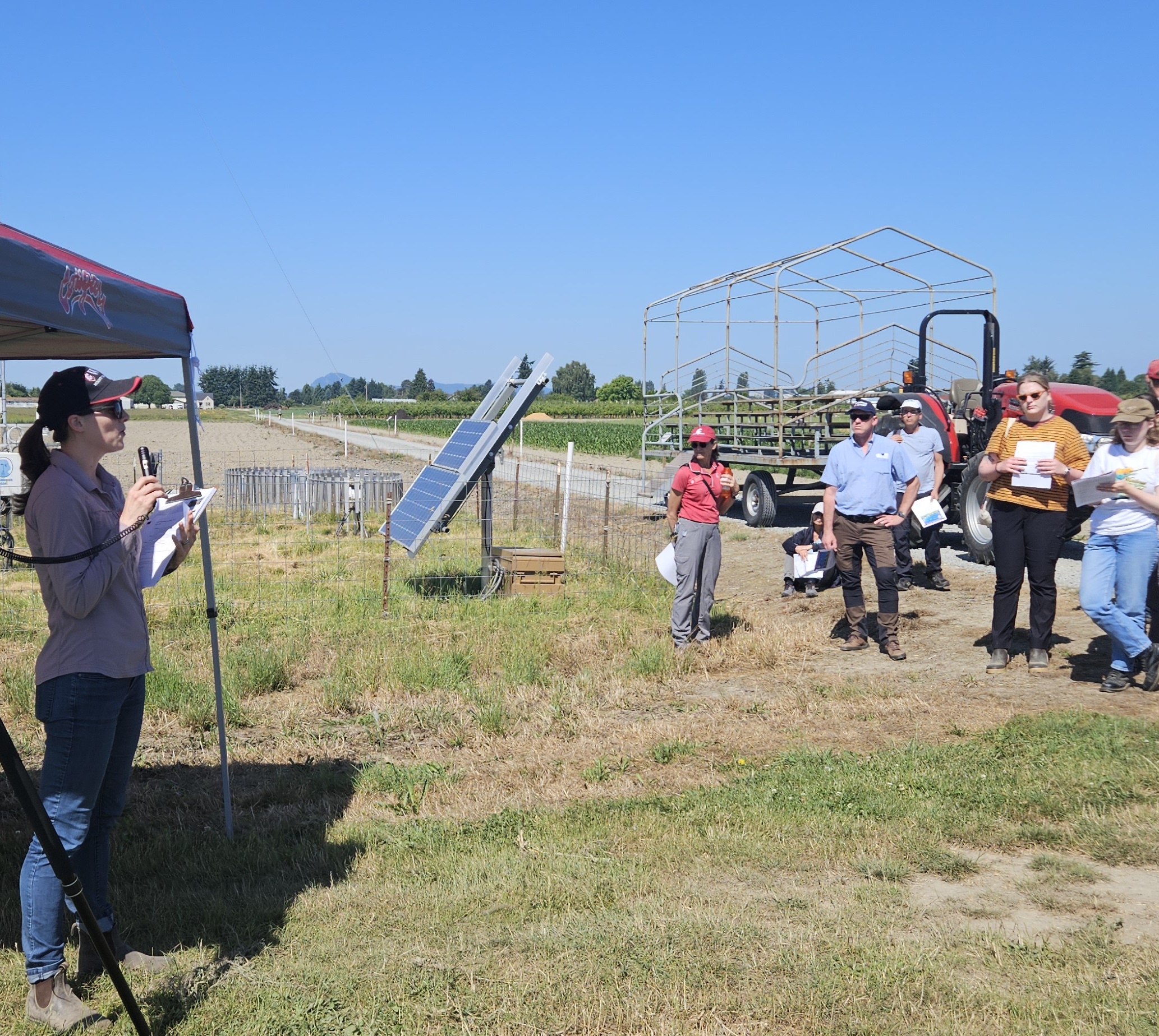 Deirdre holding a microphone and giving a talk to an outdoor audience.