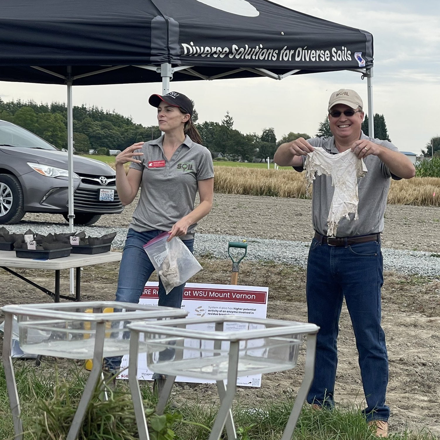 Deirdre talking out in a field with a person standing next to her holding up a decomposed tshirt.