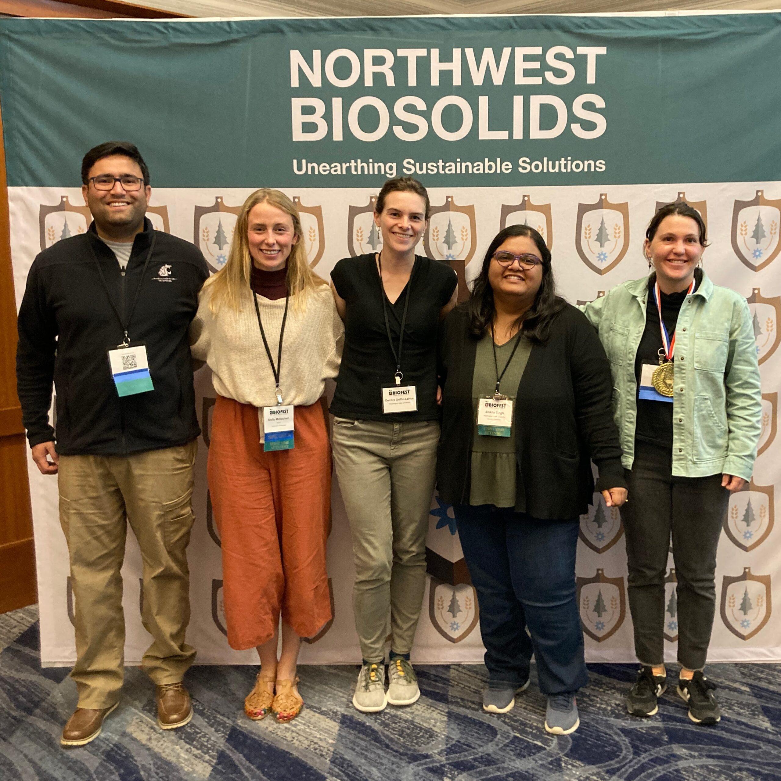 Five researchers from WSU standing together in front of a Northwest Biosolids banner. 