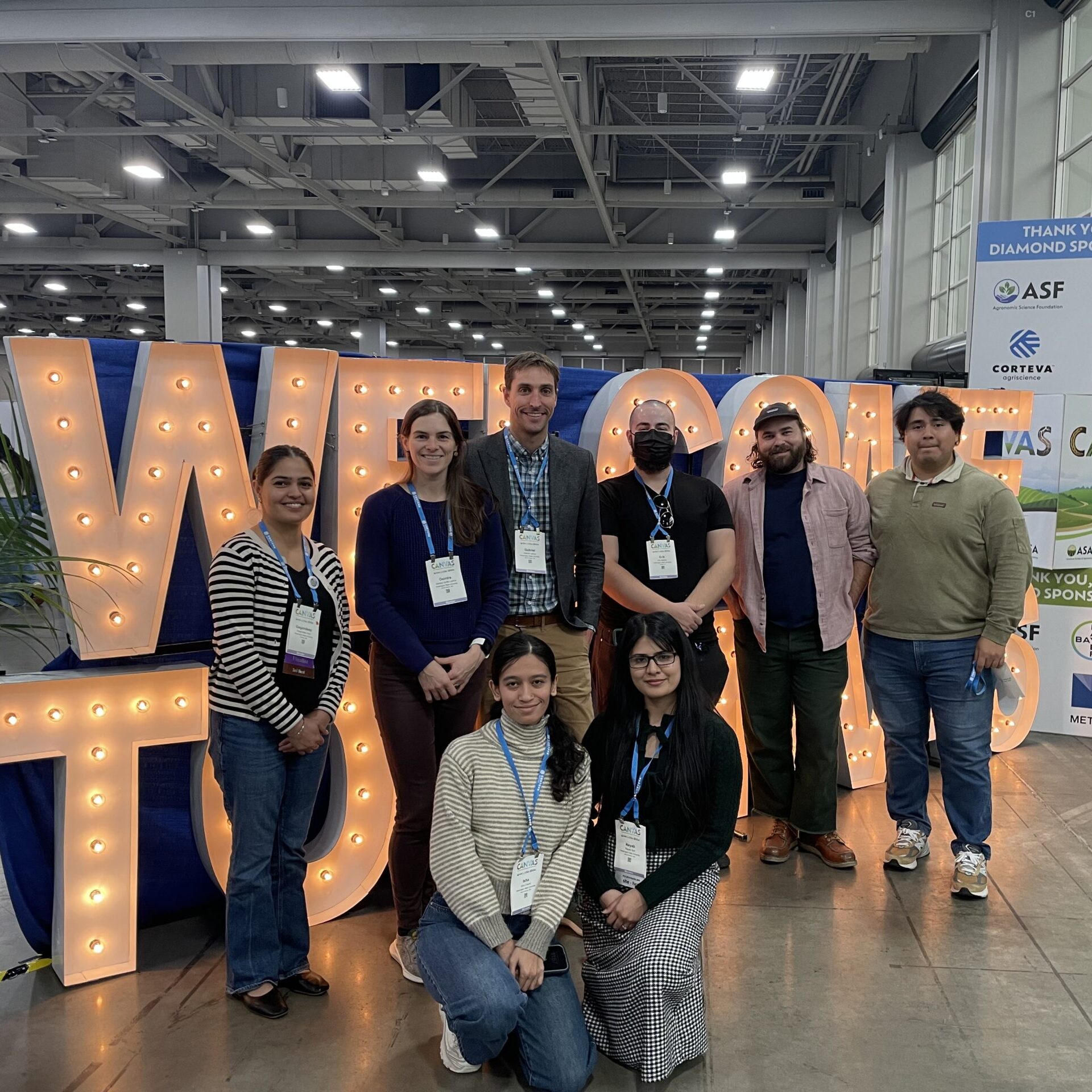 Members of the Soil Health lab at a conference, lined up in front of a lit-up sign