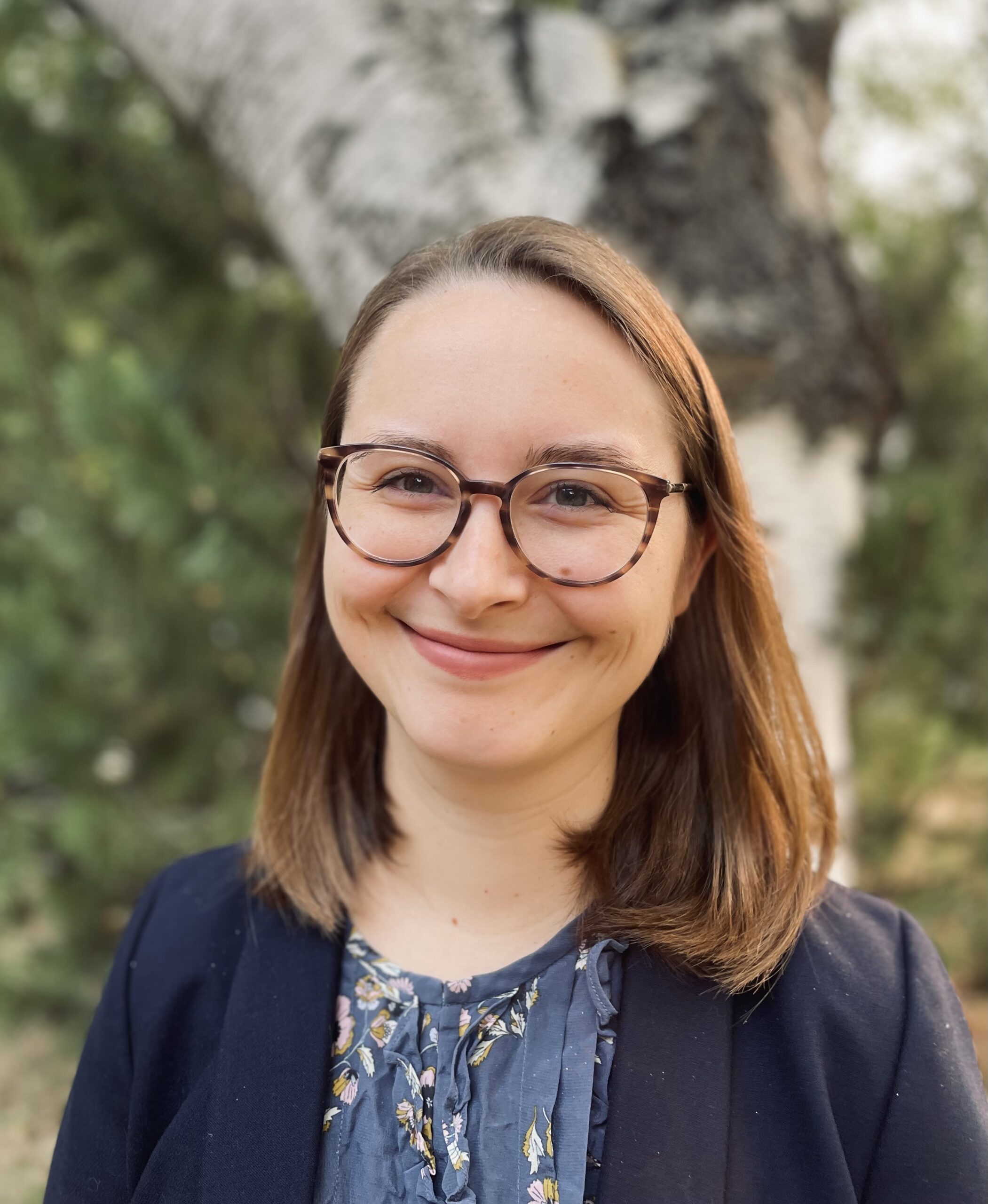 A woman with brown hair and glasses smiling.