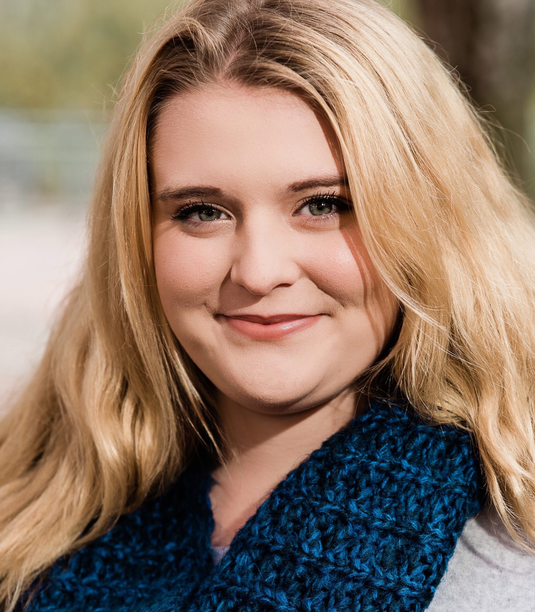 A woman with blond hair wearing a blue scarf smiling.