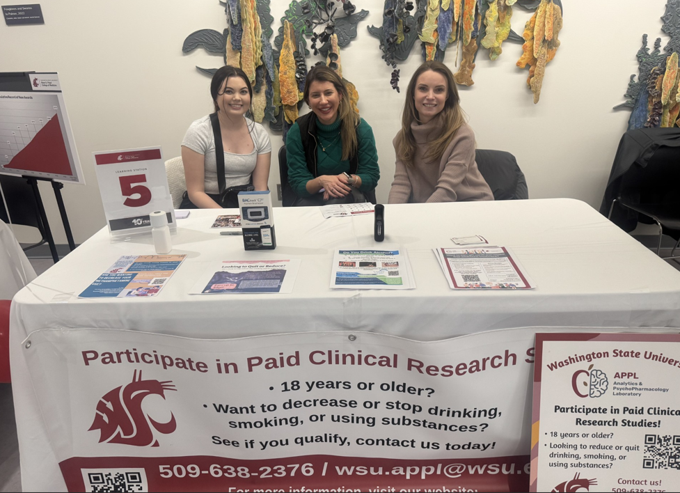 3 members from the team behind a display table at the college 10 year anniversary event.