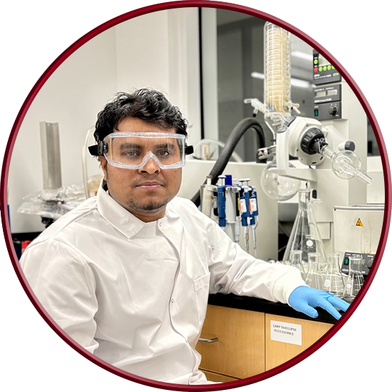 Picture of Zaman wearing full personal protective equipment in the lab sitting in front of a rotary evaporator.