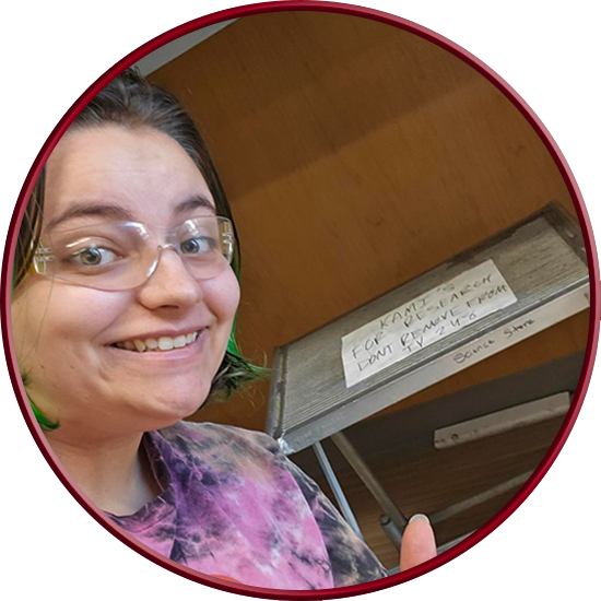 Photograph of a smiling Kami standing in from of a step stool that says 
