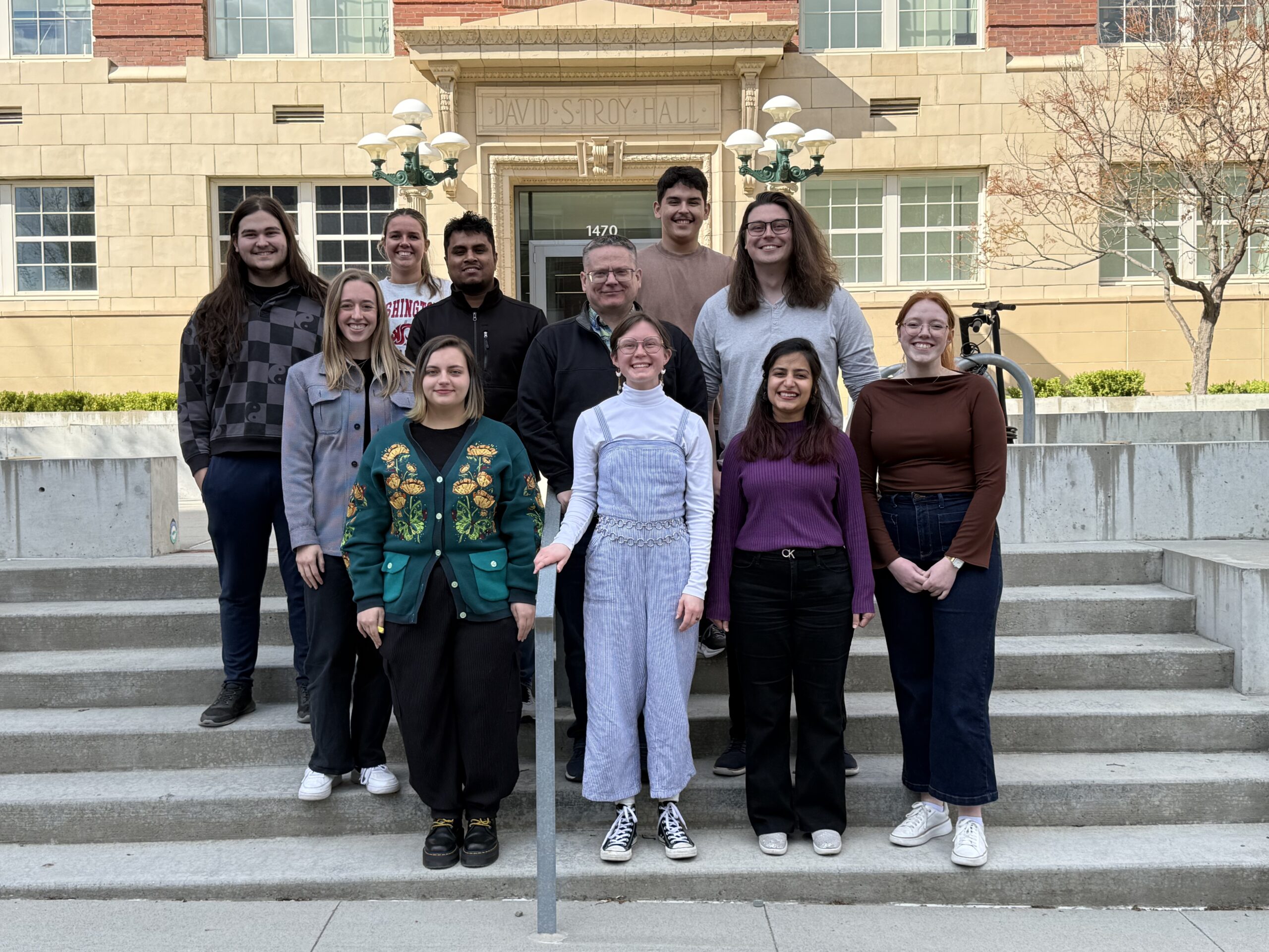 Photo of the group standing in front of Troy Hall at Washington State University on April 17, 2026. Pictured from left-to-right: (1st row): Kami, Arthur, Palak, Molly. (2nd row): Ashlyn, Zaman, Kevin, Christian. (3rd row): Thomas, Abby, Nick. Not pictured: Brianna