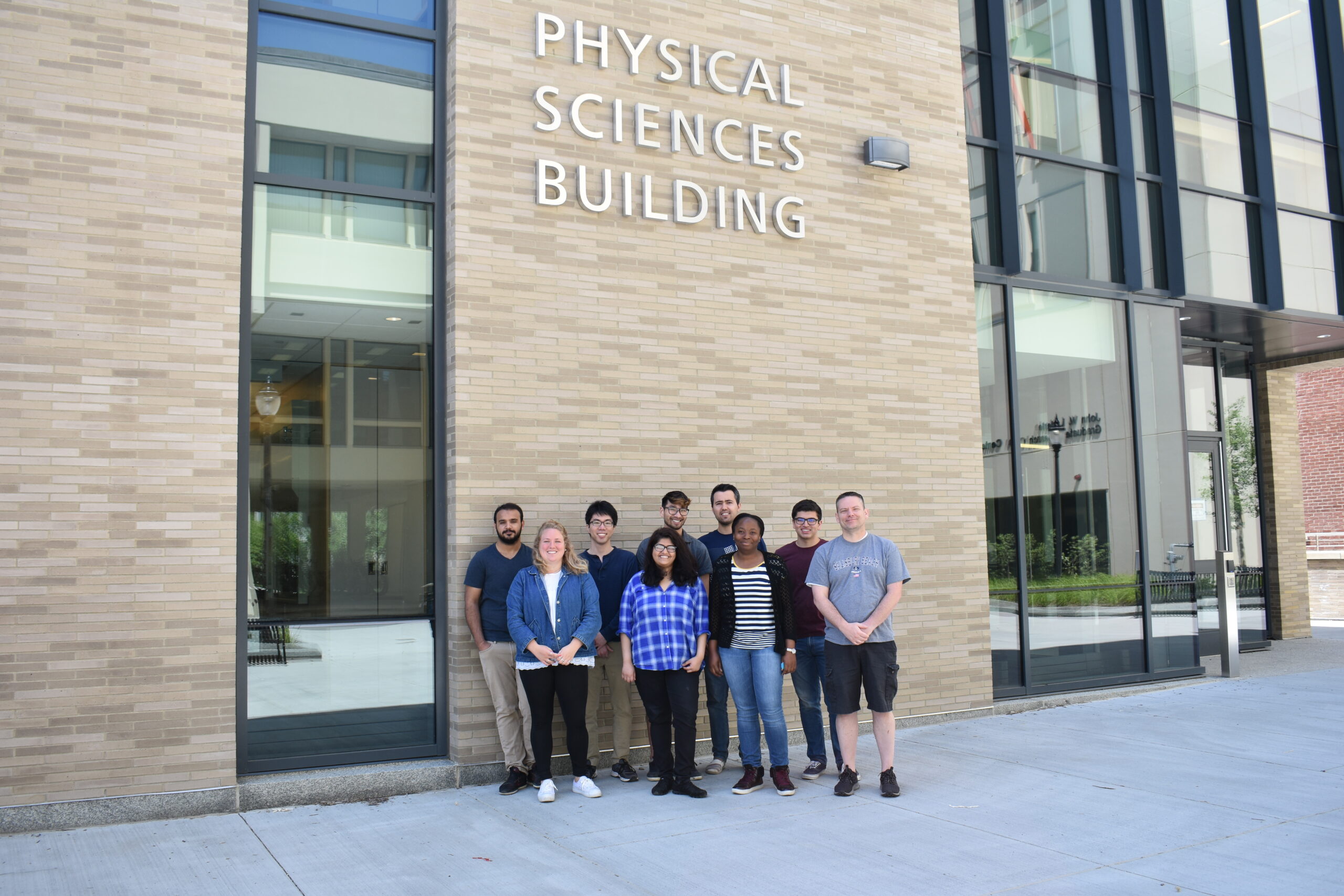 Photograph of the group standing outside of the brand new Physical Sciences Building in June 2018. Shown in the picture are (from left-to-right) Abdullah, Jill, Fumi, Haneen, William, Enes, Ekeoma, Anand, and Kevin.