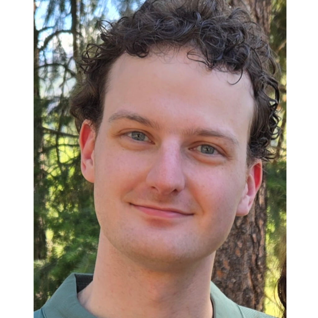 A headshot of Nathan Tuvey in green shirt in front of woods.