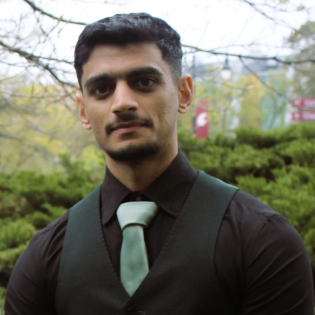 Waleed Adawi in a black shirt with green tie in front of woods