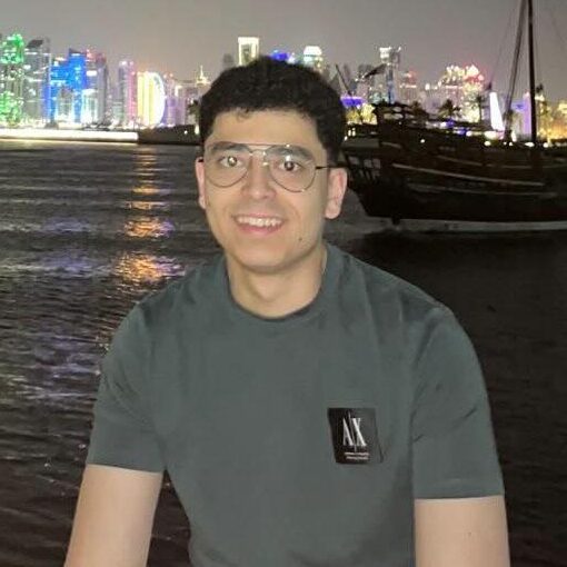 Omar Ibrahim in grey t-shirt smiling in front of a bay