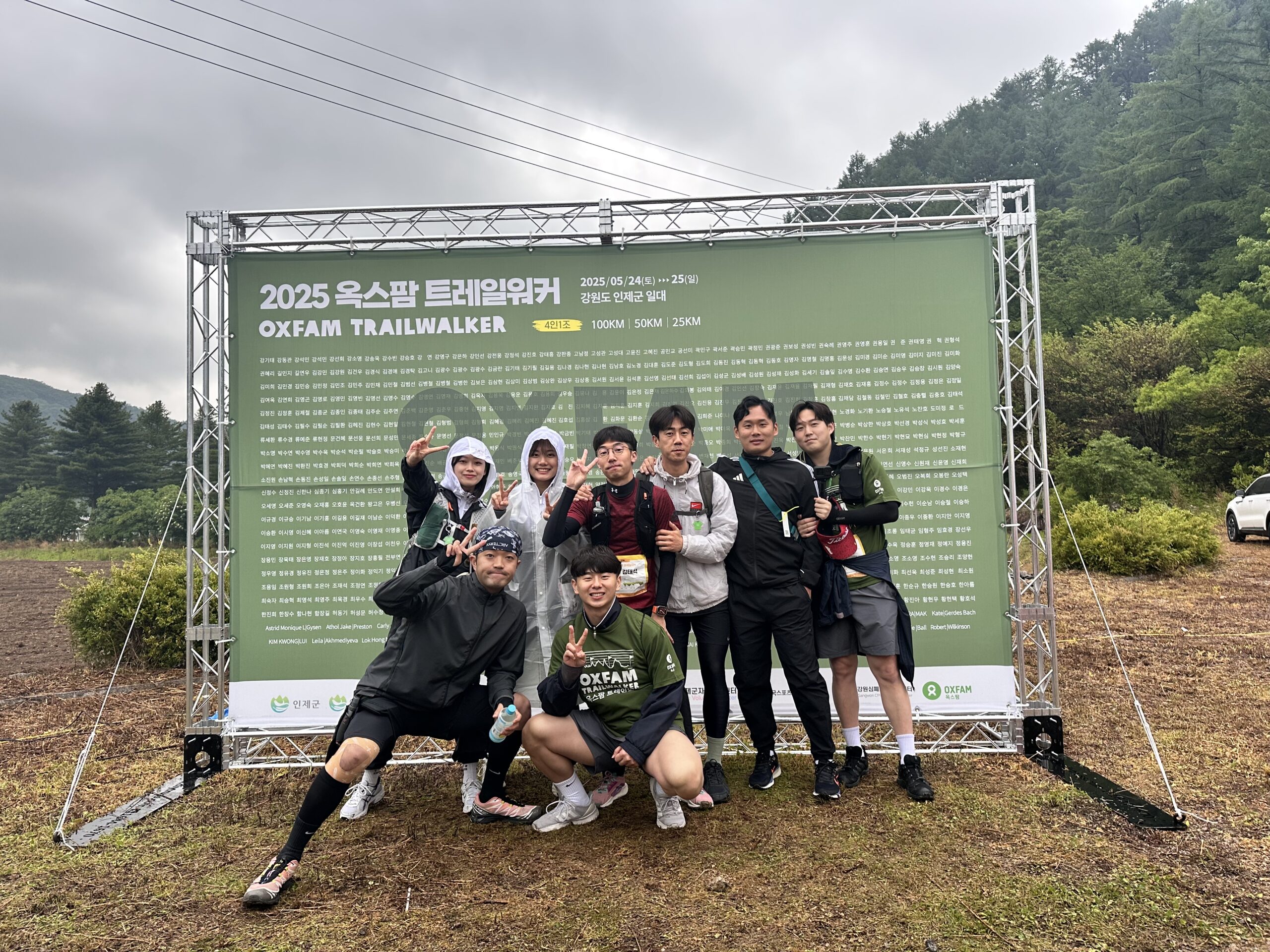 9 individuals standing in front of an OXFAM trailwalker sign in a forest