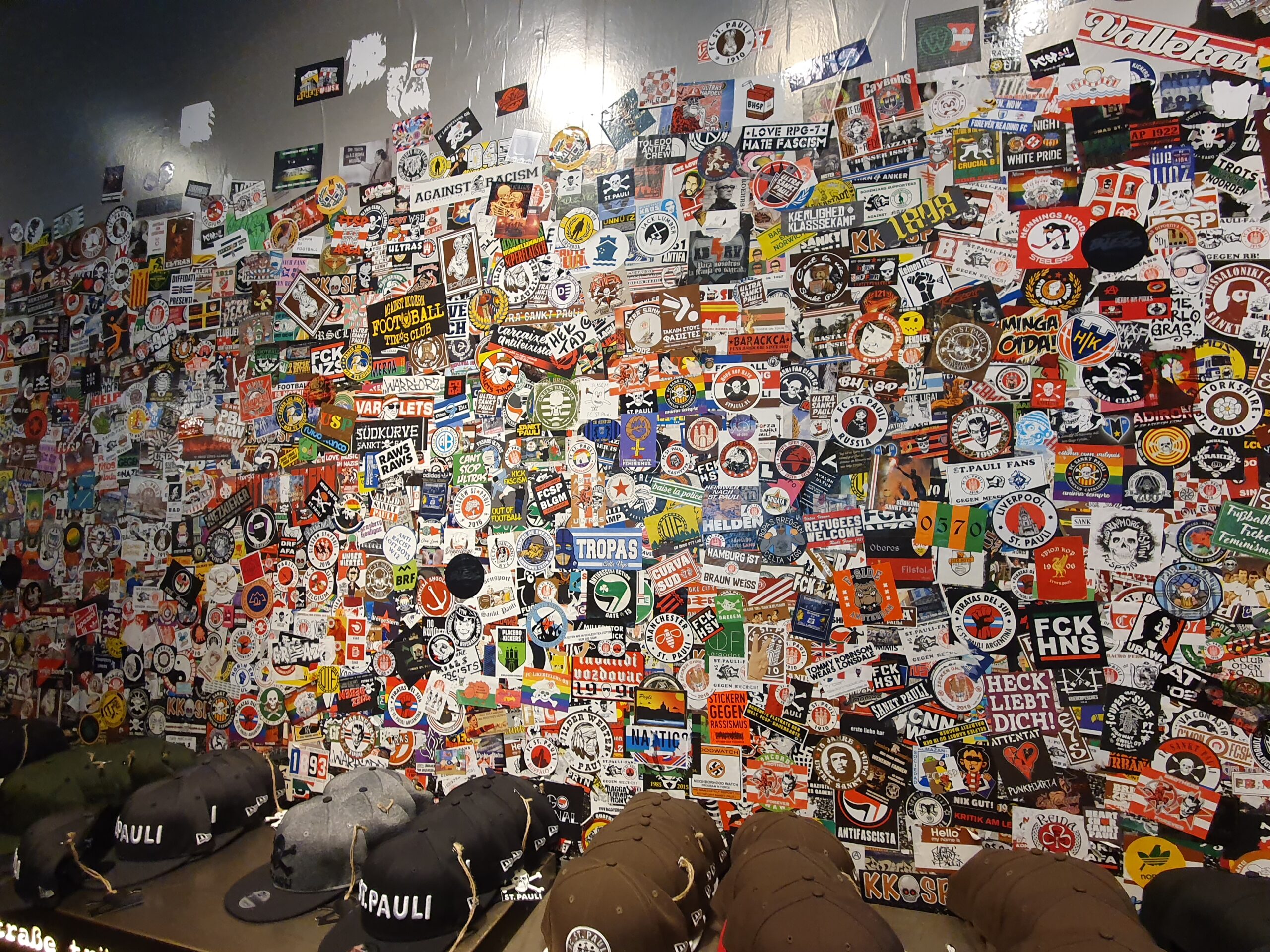 A wall of stickers on it with hats at the bottom