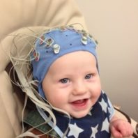 Baby boy with blue research cap on, sitting in a chair