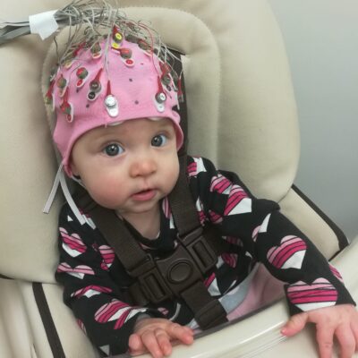 Baby girl in high chair wearing pink lab helmet