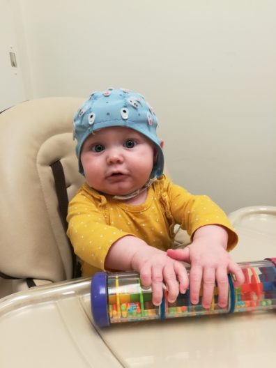 Baby boy in high chair wearing blue lab helmet and playing with toy