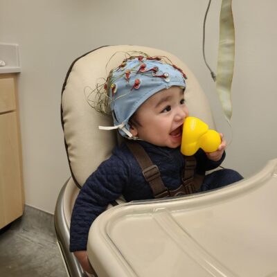 Baby boy with blue research cap on while playing with a yellow rubber duck